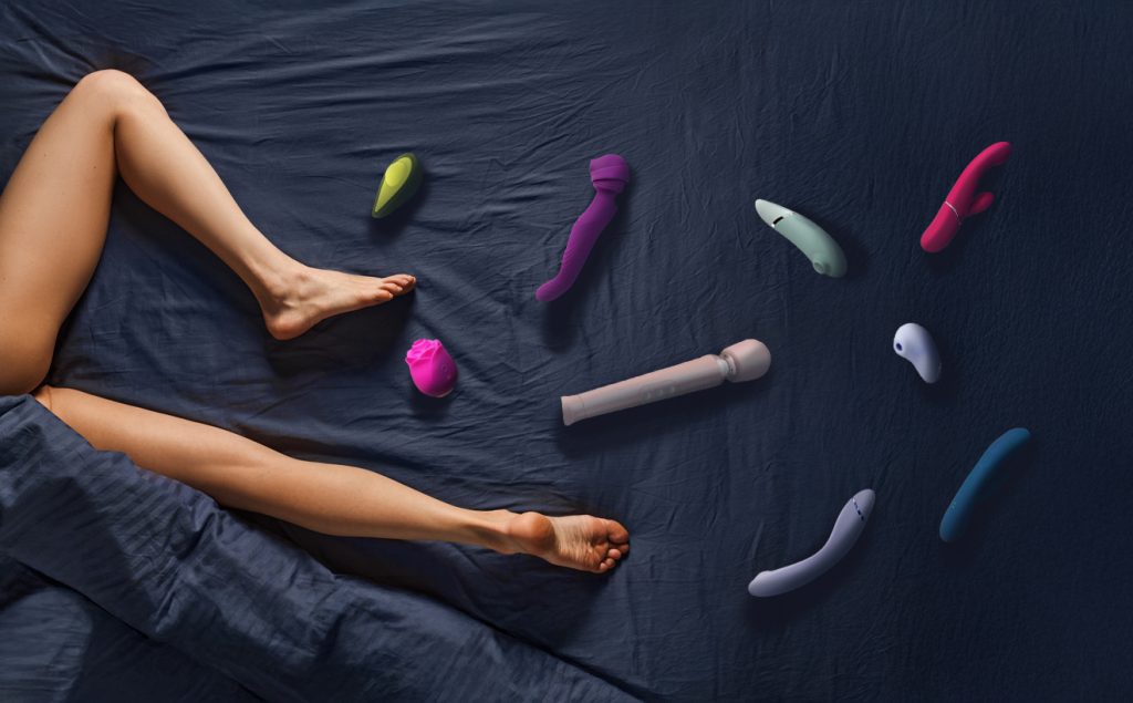 a woman's legs on a bed surrounded by adult toys.